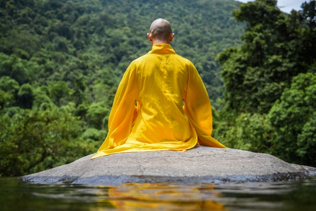 川の岩の上に座る修行僧